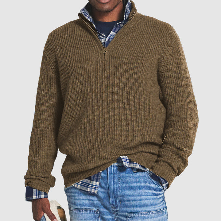 Olive green ribbed knit quarter-zip jumper with a funnel collar, layered over a blue plaid shirt and jeans.