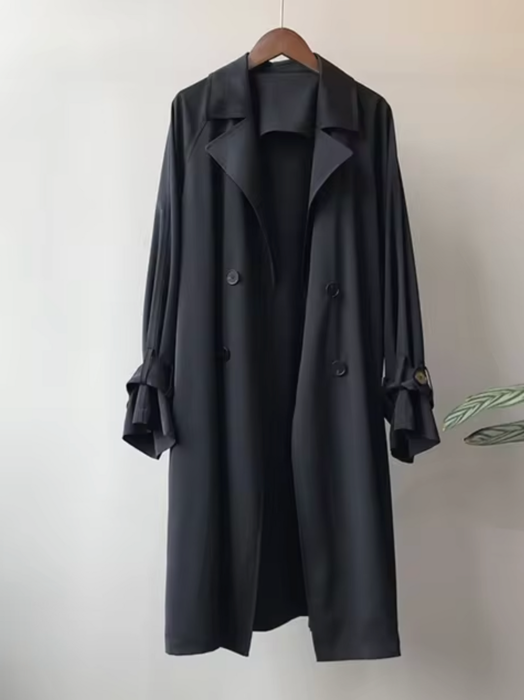 Black double-breasted waterproof trench coat with a notch lapel, long-line silhouette, and buttoned sleeve tabs.