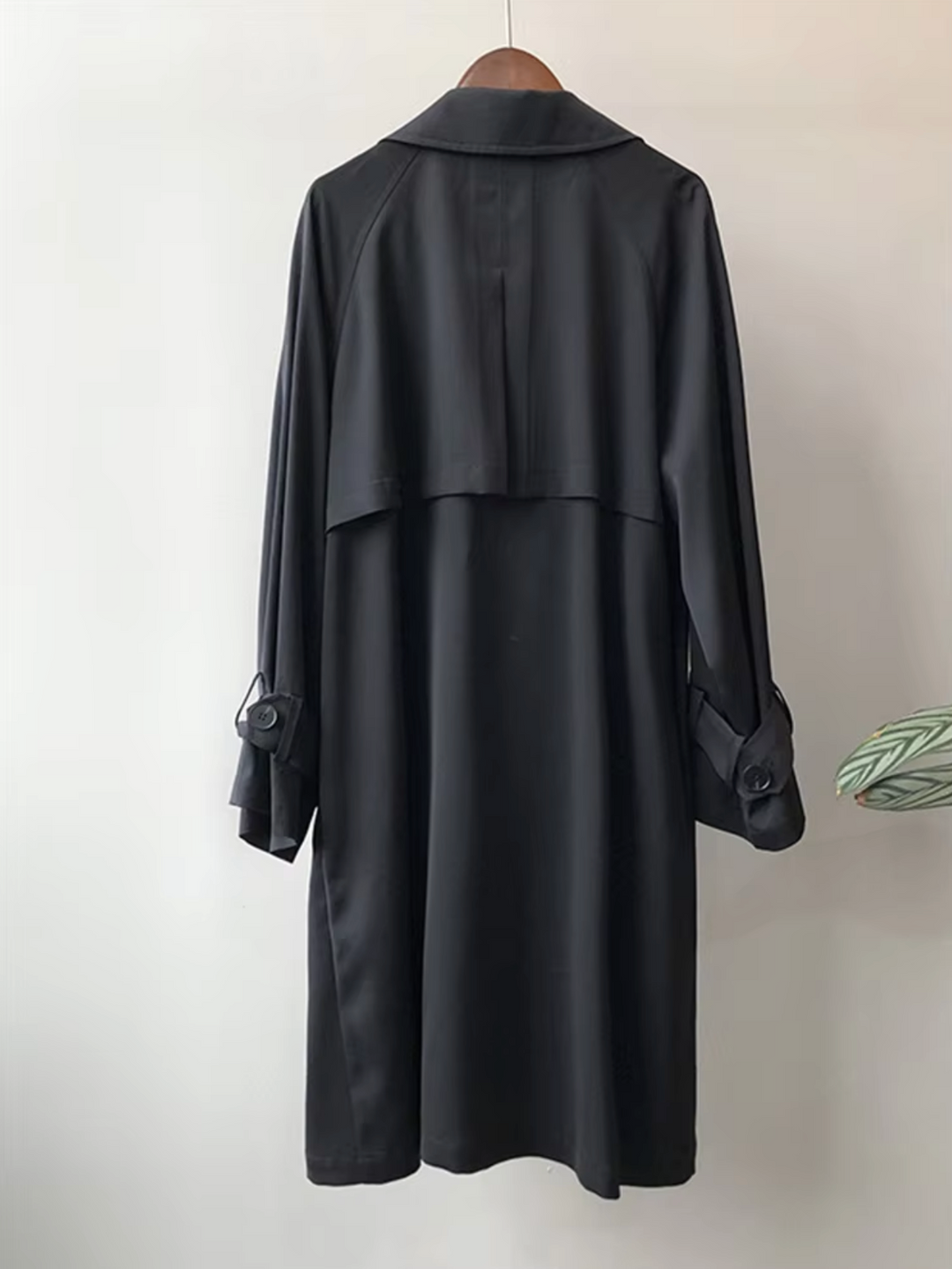 Back view of a black waterproof trench coat featuring a longline silhouette, storm flap, and buttoned sleeve tabs.