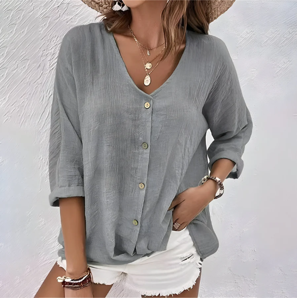 Grey linen-look V-neck blouse with a button-up front and relaxed roll-up sleeves worn with white shorts.