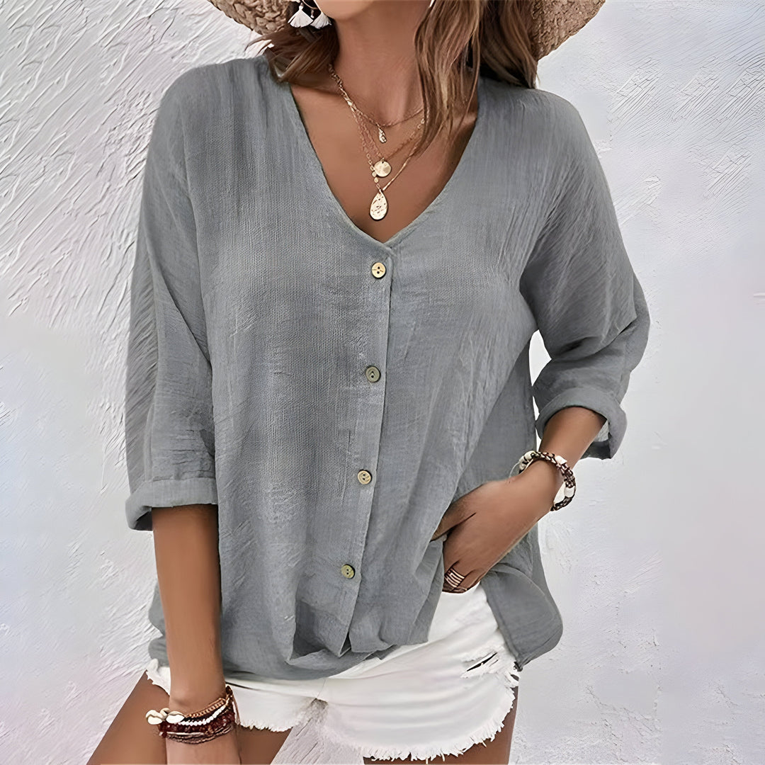 Grey linen-look V-neck blouse with a button-up front and relaxed roll-up sleeves, styled with white shorts.