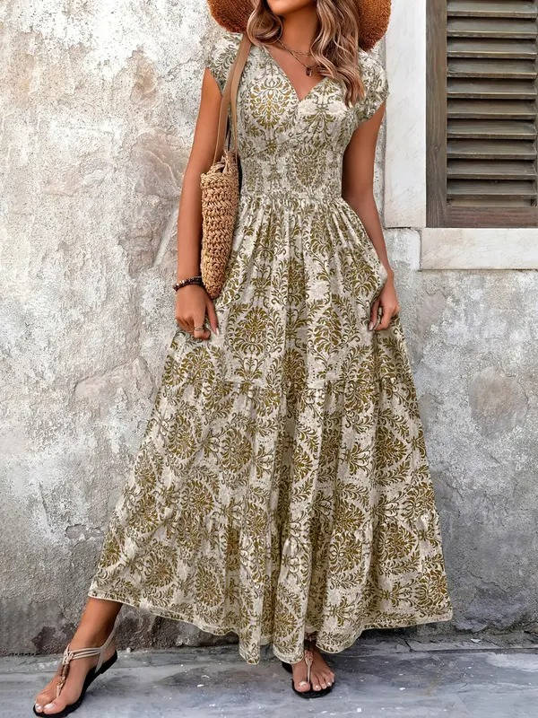 Boho floral maxi dress with a V-neck, smocked bodice, and tiered skirt in olive green and cream, paired with a straw bag.