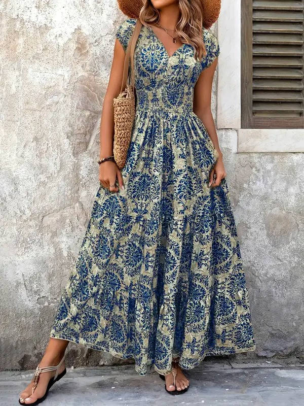 Blue and beige floral print boho maxi dress with a V-neck, smocked bodice, and tiered skirt, styled with a straw bag and hat.