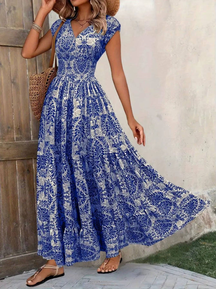 Blue and white floral boho maxi dress with a smocked bodice, V-neckline, cap sleeves, and a tiered, flowing skirt.