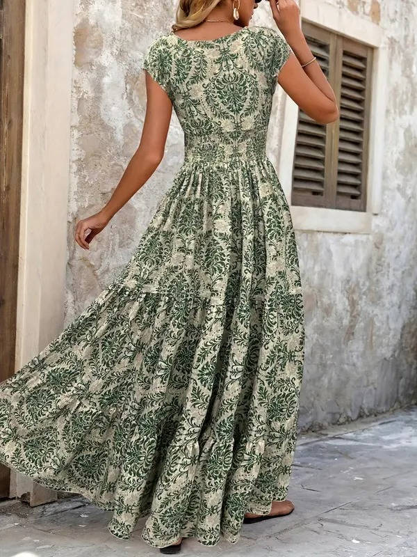Woman wearing a green and cream floral print boho maxi dress with a smocked bodice, cap sleeves, and a tiered, flowing skirt.